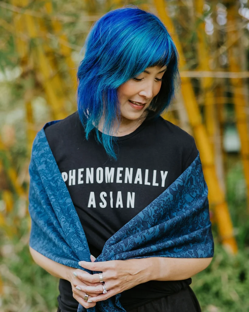 Asian woman with blue hair wearing a black T-shirt that says Phenomenally Asian and a blue kimono fabric scarf.