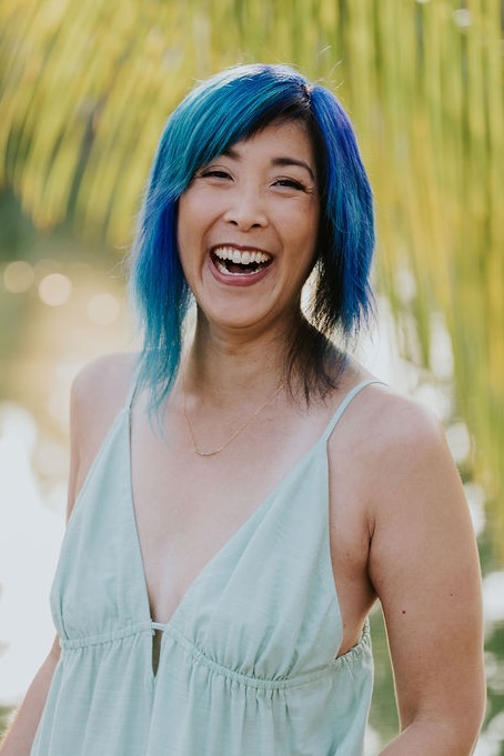 Headshot of Jenn Ayako Lee in a spaghetti strap mint green dress with palm fronds in the background.