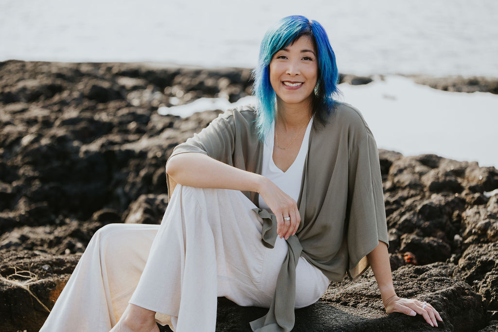 Jenn Ayako Lee sitting on lava rocks by the ocean.