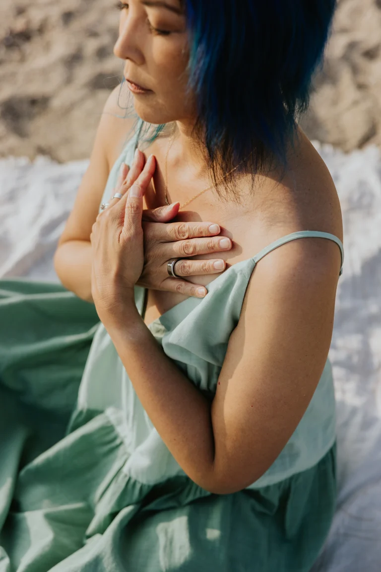 Woman sitting on beach with eyes closed and hands in butterfly pose palms on heart